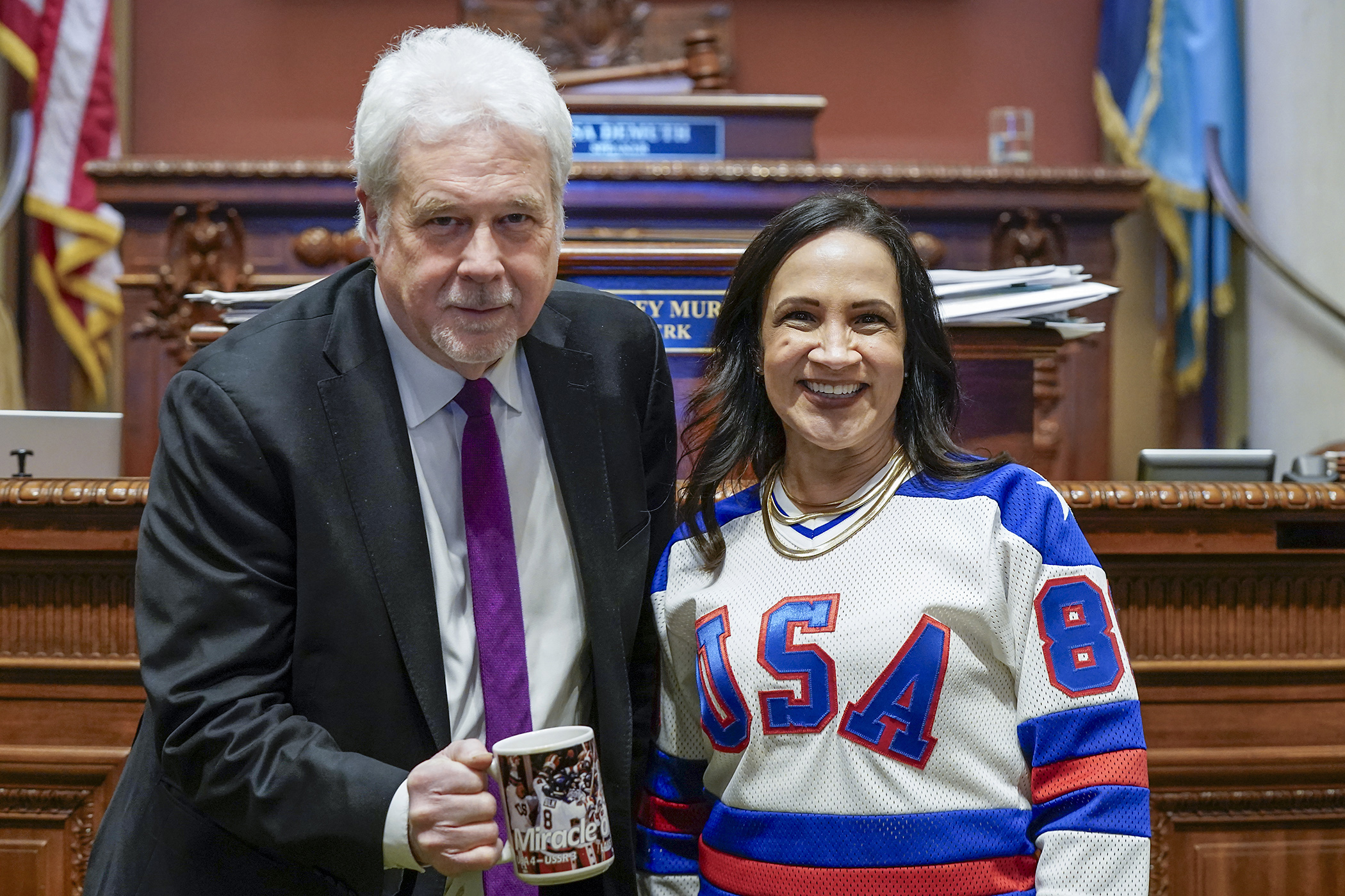 Chief Clerk Patrick Murphy and House Speaker Lisa Demuth show off their U.S.A. Olympic hockey spirit on the House Floor Feb. 23 with a vintage coffee mug and vintage hockey jersey from the 1980 gold medal team. (Photo by Michele Jokinen)